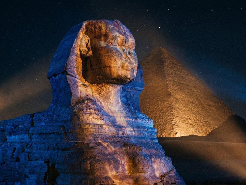 Colored stage lighting washes over the Great Sphinx and the pyramids beyond during the evening performance.