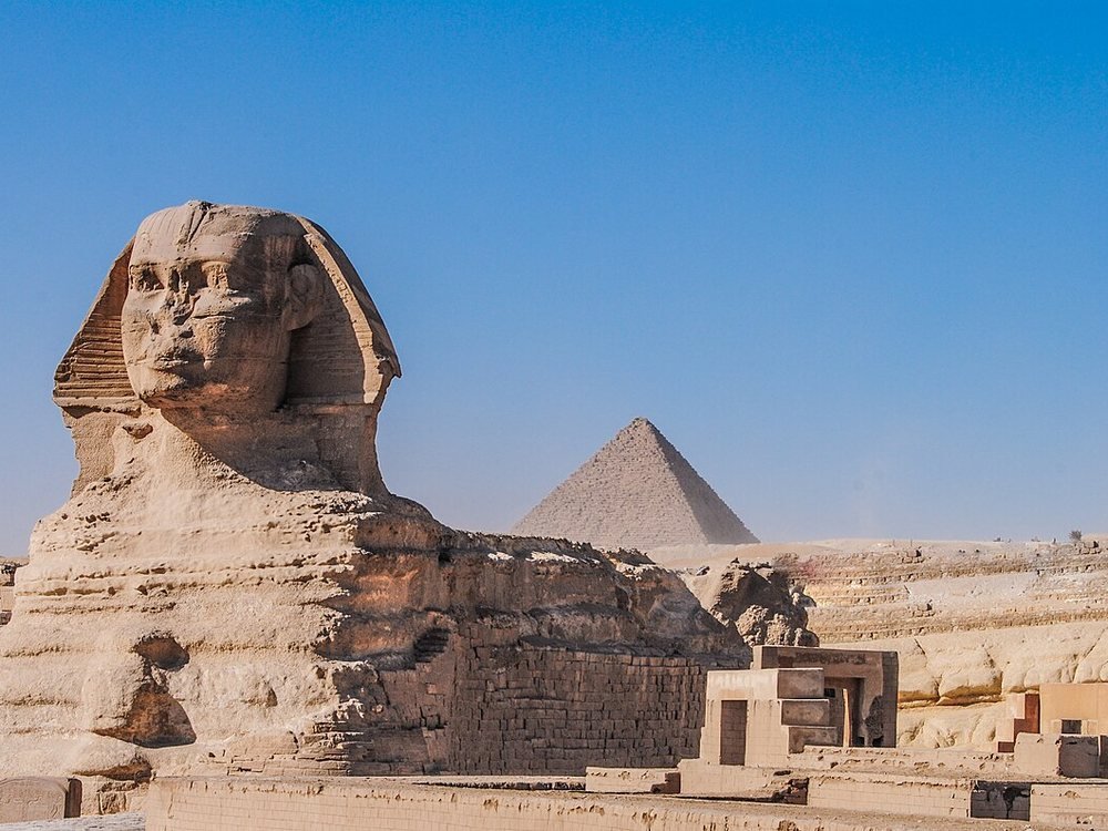 The Great Sphinx of Giza, carved from a single limestone outcrop, with the pyramids beyond.